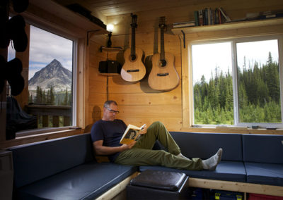 A man laying down on the couch and reading a book in the living room of the Mallard Mountain Lodge.