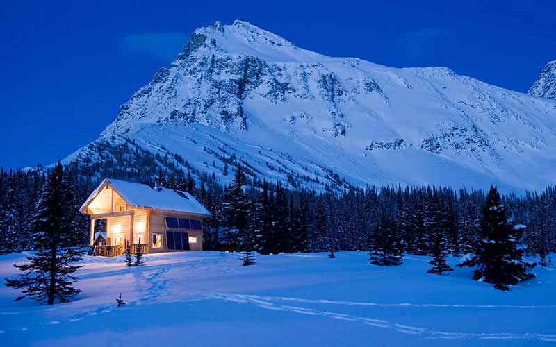 A photo of the Mallard Mountain Lodge surrounded by the snowy Canadian Rocky Mountains at night. 
