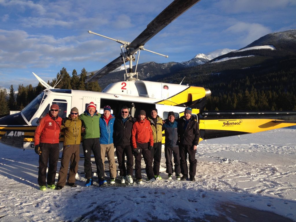 Group of men posing for photo in front of helicopter on snow