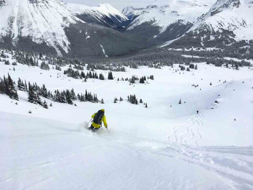 man skiing powder down a slope towards a mountain valley